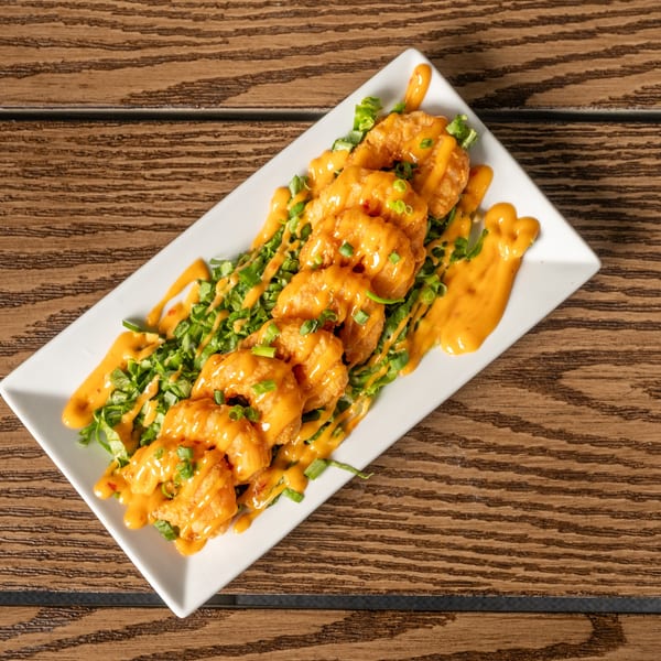 Crispy fried shrimp drizzled with orange sauce and garnished with green onions on a white plate.