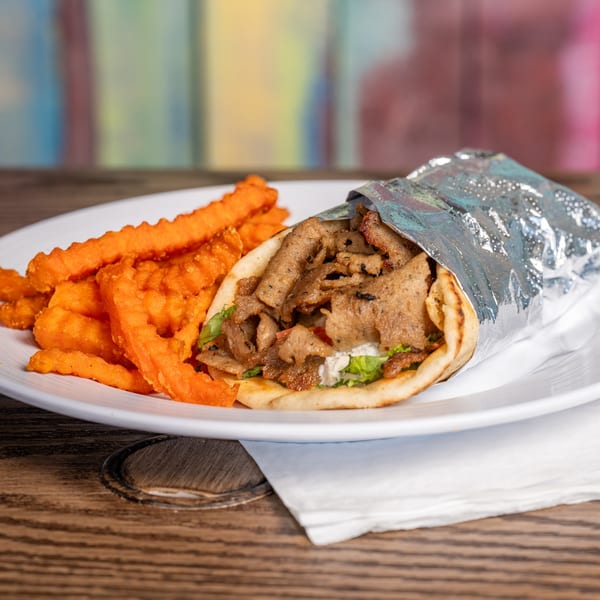 A gyro with meat, lettuce, and sauce, wrapped in foil, served with sweet potato fries.