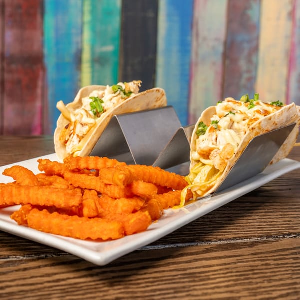 Two chicken tacos with creamy sauce and green onions, served with a side of sweet potato fries.