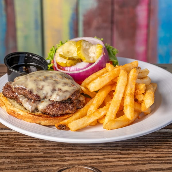 A double cheeseburger with melted cheese, fries, and a side of pickles and onions on a white plate.