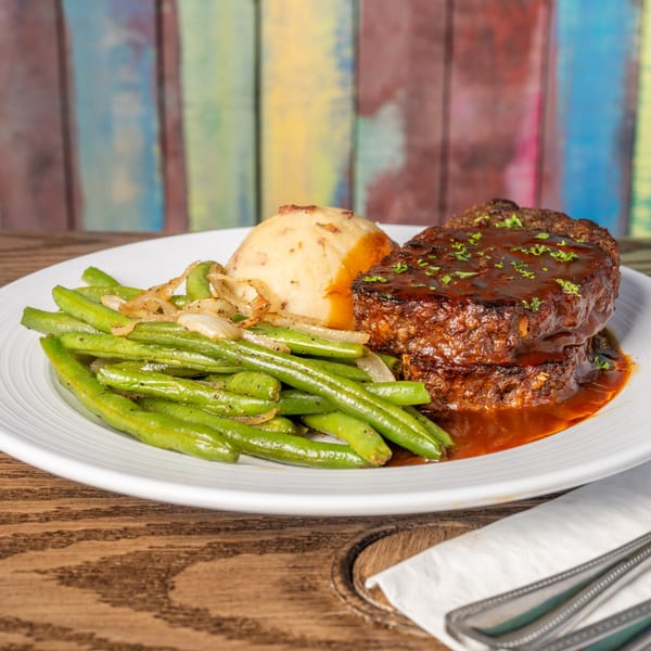 Meatloaf with mashed potatoes and green beans on a white plate at 2 Creeks Bar & Grill.