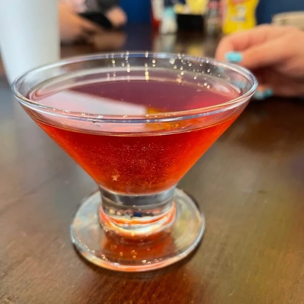 A vibrant red cocktail in a martini glass sits on a wooden table at 2 Creeks Bar & Grill.