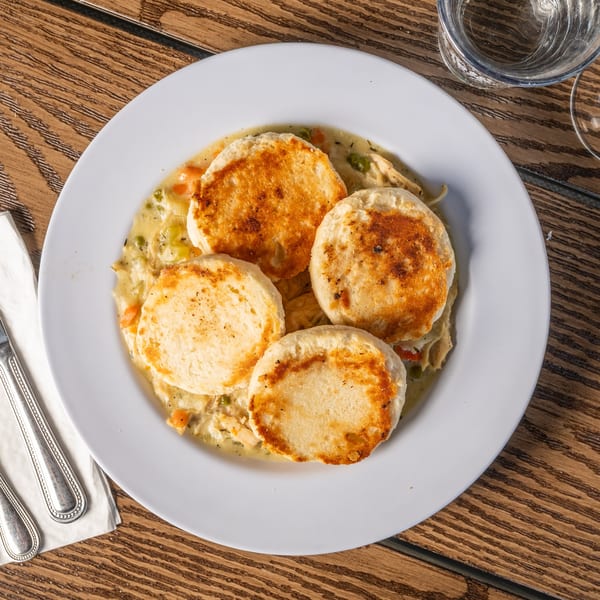 Chicken pot pie with four golden-brown biscuits on top, served on a white plate.