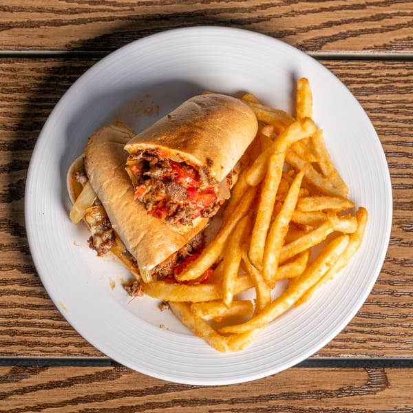 A cheesesteak sandwich with peppers and onions, served with a side of golden french fries.